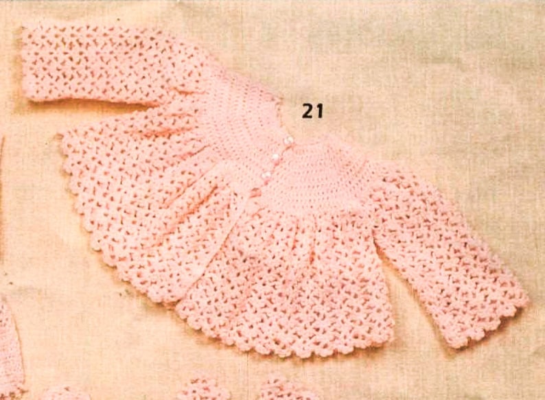 May include: A pink crocheted baby cardigan with long sleeves and a button closure. The cardigan has a scalloped edge and a delicate pattern.