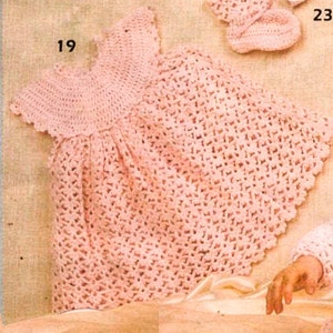 May include: A pink crocheted baby dress with a scalloped edge. The dress has a round neckline and short sleeves.
