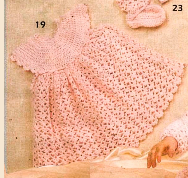 May include: A pink crocheted baby dress with a scalloped edge. The dress has a round neckline and short sleeves.