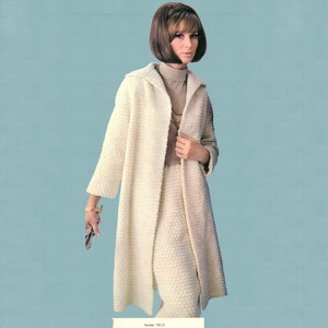 May include: A woman in a cream-coloured, textured coat and skirt ensemble. The long coat features a collar and is open at the front. The skirt is knee-length. She is also wearing a turtleneck and a necklace. The background is a light blue.