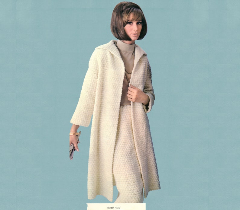 May include: A woman in a cream-coloured, textured coat and skirt ensemble. The long coat features a collar and is open at the front. The skirt is knee-length. She is also wearing a turtleneck and a necklace. The background is a light blue.