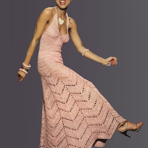 Puede incluir: Un vestido largo de crochet rosa claro con un patrón de chevrón. El vestido tiene una falda larga fluida y está adornado con pulseras y un collar a juego. La modelo lleva tacones altos dorados.
