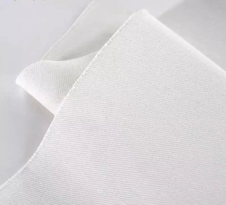May include: White fabric with a textured surface. The fabric is folded over itself, showing the underside of the fabric.