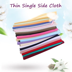 May include: A stack of 26S fine cotton thin single side cloth in a variety of colours, including white, black, red, blue, and green. The fabric is soft and smooth, and it is ideal for a range of sewing projects.