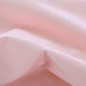 May include: A close-up of a soft, pale pink fabric with a smooth, even texture. The fabric is folded and draped, creating a gentle, flowing effect.