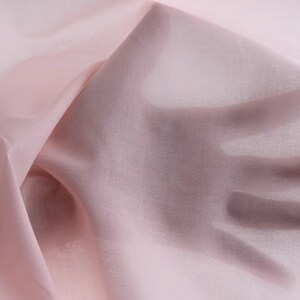 May include: A pale pink sheer fabric, draped and held in a hand. The fabric is soft and delicate, with a subtle sheen.