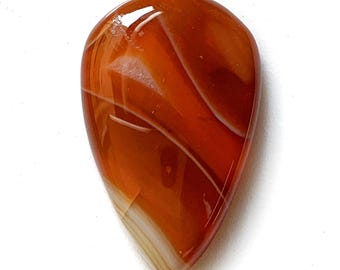 May include: A teardrop-shaped gemstone with a polished surface. The stone features bands of orange, brown, and white, creating a natural, swirling pattern. The gemstone is set against a white background.