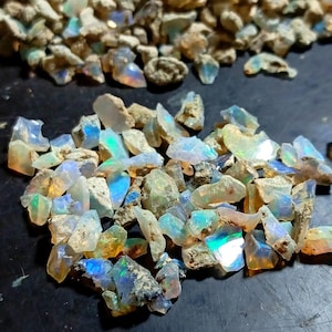 Peut inclure: Un ensemble de pierres d'opale brutes, présentant une variété de couleurs, notamment le bleu, le vert et l'orange. Les opales sont taillées grossièrement et ont un aspect naturel et terreux. Les pierres précieuses sont dispersées sur une surface sombre.
