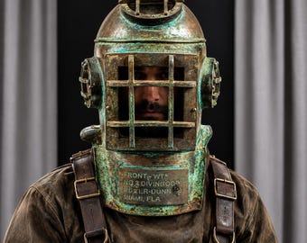 May include: A vintage-style copper and brass diving helmet with a weathered green patina. The helmet features a front viewing port with a metal grid, side ports, and a top handle. The front plate is embossed with the text FRONT-WT NO 3 DIVINGBOOD WD ER-DUNN MIAMI, FLA.