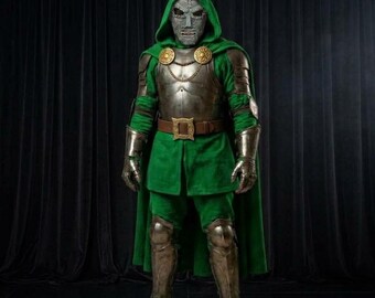 May include: A full-body costume featuring a metallic silver mask with a textured surface, a green hooded tunic, and matching green trousers. The ensemble includes a dark brown leather belt with a gold buckle, gold circular shoulder accents, and metallic silver gauntlets and greaves.