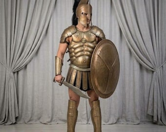 May include: A bronze-colored Spartan-style armor set featuring a Corinthian helmet with a black crest, a muscular breastplate with a central lion emblem, a skirt of leather-like tassets, arm guards, greaves, a round shield, and a short sword.