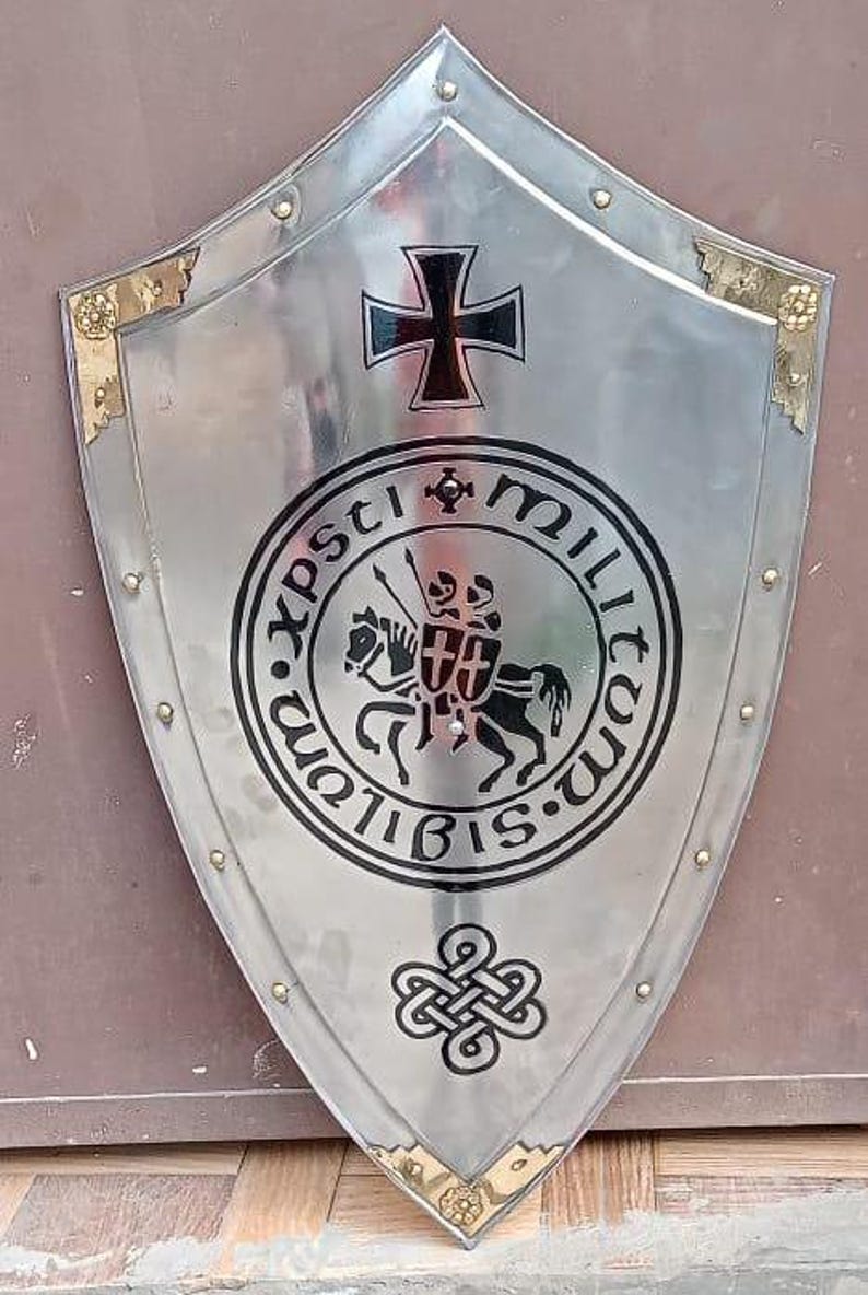 May include: A polished silver-tone metal shield featuring a central black graphic of two knights on a horse, surrounded by the text Sigillum Militum Xpsti. Above is a black cross, and below is a decorative knot design with gold-tone corner accents.