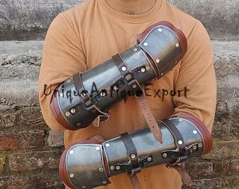 May include: A pair of metal arm guards with brown leather straps. The guards are made of metal and have a silver finish. The straps are adjustable and can be worn on either arm.
