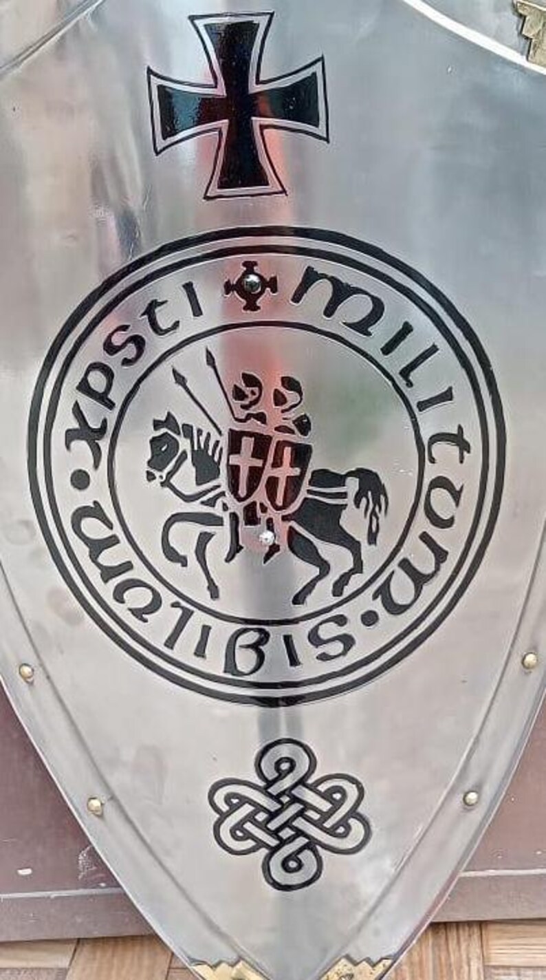 May include: A polished silver-toned metal shield featuring a black Iron Cross at the top. The center displays a circular emblem with the Latin text 'Sigillum Militum Xpsti' surrounding an engraving of two knights on a single horse. A knot design sits below.