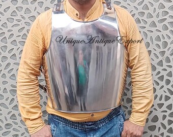 May include: A polished, silver-colored breastplate with leather straps. The breastplate has a reflective surface and is worn over a yellow long-sleeved shirt and blue jeans. The text "Unique Antique Export" is visible on the breastplate.