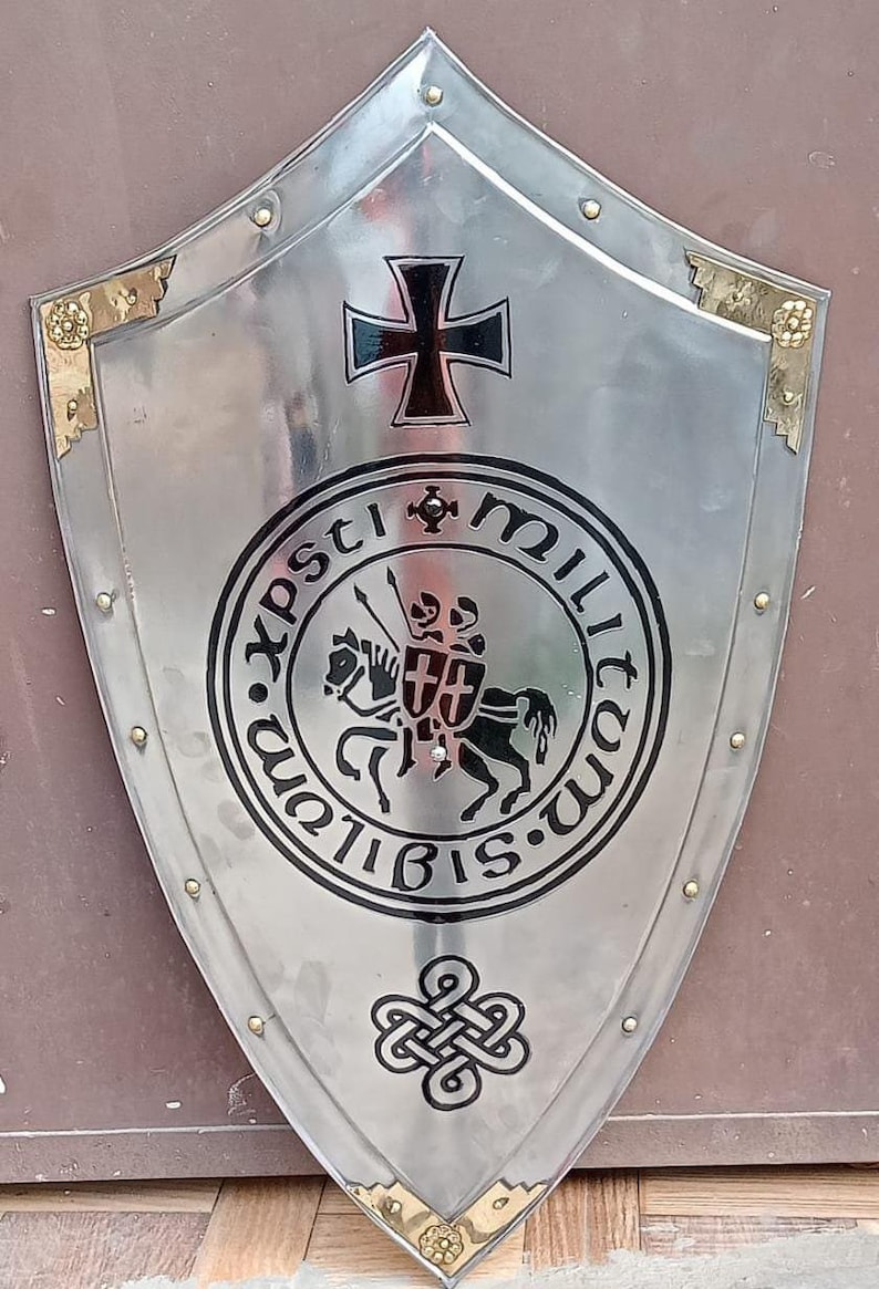 May include: A polished silver-tone metal heater shield featuring a black iron cross at the top, a central circular emblem depicting two knights on a horse with the text "xpsti militum sigillum", and a black Celtic knot design at the bottom.