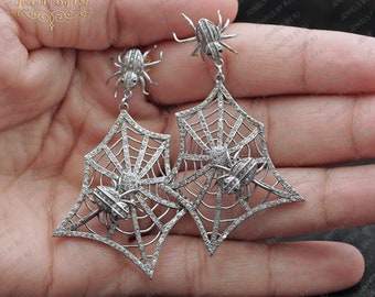 May include: A pair of silver spider web earrings with diamond accents. Each earring features a spider web design with three spiders crawling on it.