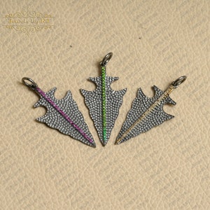May include: Three silver arrowhead pendants with a pave setting of clear and colored gemstones. The arrowheads are set with a single line of pink, green, and yellow gemstones.