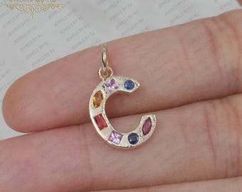 以下が含まれることがあります： Cの字型の金製のチャームで、カラフルな宝石が金属に埋め込まれています。宝石は赤、オレンジ、黄色、緑、青、紫です。