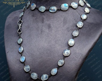 May include: A necklace featuring oval-shaped, iridescent moonstone gemstones set in a dark metal chain. The necklace is displayed on a gray mannequin bust. The jewelry is from Jewels By RJ.