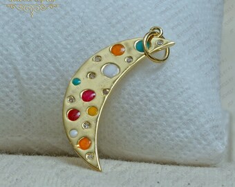 Könnte beinhalten: Ein goldener Halbmond-Anhänger mit einem bunten Emaille-Design. Der Anhänger ist mit kleinen, runden, mehrfarbigen Emaille-Punkten und einem größeren weißen Emaille-Punkt verziert. Der Anhänger hat eine kleine goldene Öse oben zum Anbringen an einer Kette.