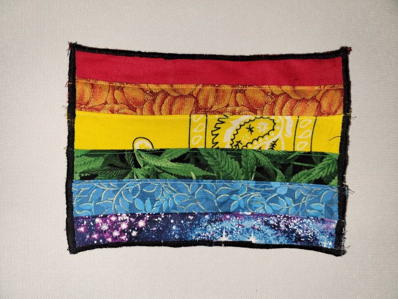 K&ouml;nnte beinhalten: Ein farbenfroher Stoff-Patch mit einem Regenbogen-Design. Der Patch besteht aus verschiedenen Stoffen, die zusammengen&auml;ht wurden, um ein gestreiftes Muster zu erzeugen. Die Farben der Streifen sind rot, orange, gelb, gr&uuml;n, blau und lila.