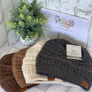 May include: Four alpaca wool knit beanies in brown, beige, and gray. The gray beanie has a label that reads "Mother Nature's Finest Rider USA Alpaca Made in the USA with US Grown Alpaca".