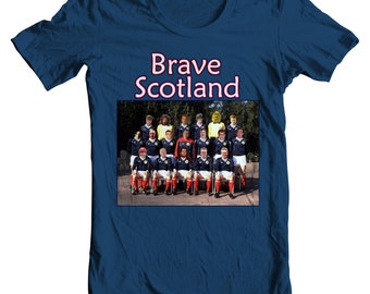 Puede incluir: Una camiseta azul marino con la frase "Brave Scotland" en blanco con un borde rojo. La camiseta muestra una foto de equipo vintage de un grupo de personas con uniformes a juego.