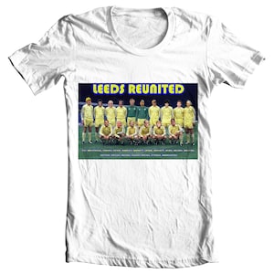 Puede incluir: Una camiseta blanca con una foto vintage de un equipo de fútbol con uniformes amarillos y azules. El texto "LEEDS REUNITED" está impreso en amarillo y azul en la foto. Los nombres de los jugadores están listados debajo de la foto.