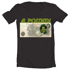 May include: A black t-shirt featuring a green and white image of a one pound note from the Bank of England. The note depicts a man with a moustache and the text "£ POUND!" in green.