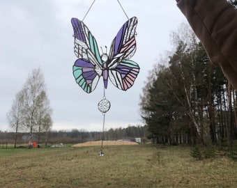 May include: A stained glass butterfly wind chime with purple, pink, and green accents. The butterfly is hanging from a silver chain with a crystal ball at the bottom.