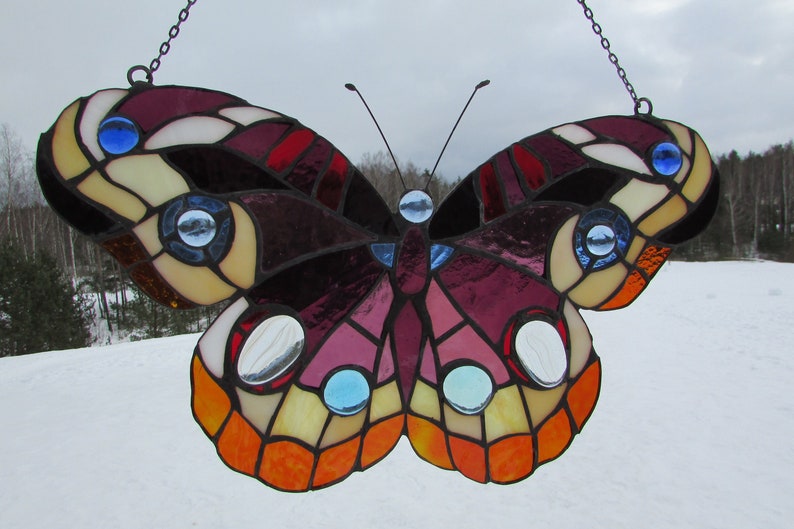 May include: A stained glass butterfly with purple, red, orange, yellow, and blue accents. The butterfly is hanging from a chain.