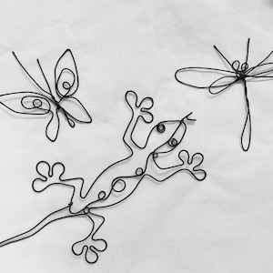 May include: Three wire sculptures of a butterfly, dragonfly, and a gecko. The sculptures are made of black wire and are arranged on a white background.