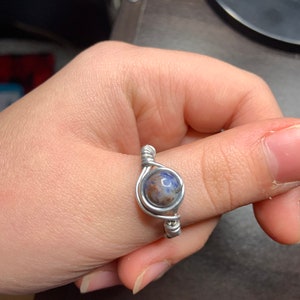 Może przedstawiać: Srebrny pierścionek owinięty drutem z niebieskim i brązowym kamieniem.