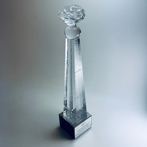 May include: A clear glass award with a textured, cloud-like top and a spherical midsection. The tall, rectangular body tapers to a black base with a small plaque. The award is approximately 12 inches tall.