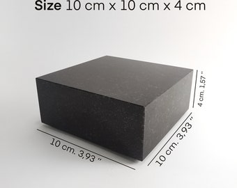 Puede incluir: Un bloque cuadrado negro sólido con textura moteada. El objeto está etiquetado con el texto Size 10 cm x 10 cm x 4 cm, junto con líneas de dimensión que indican medidas de 10 cm, 3,93 pulgadas y 4 cm, 1,57 pulgadas en sus lados.