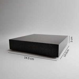 Könnte beinhalten: Ein massiver, schwarzer, rechteckiger Block mit einer Länge von 14,5 cm, einer Breite von 14,5 cm und einer Höhe von 3 cm. Die Oberfläche hat ein leicht strukturiertes Aussehen. Es ist ein Präsentationsständer oder eine Plattform.