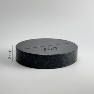 Peut inclure: Un dessous de verre rond en pierre gris foncé. Le dessous de verre mesure 2 cm d'épaisseur et 9,4 cm de diamètre. La surface a une texture mouchetée. L'objet est solide et durable.