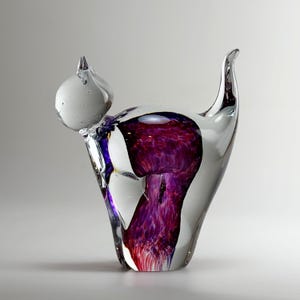 Może przedstawiać: Przezroczysta szklana rzeźba kota z białą głową i korpusem wypełnionym żywym fioletowo-czerwonym wzorem. Rzeźba ma zakrzywiony ogon i elegancki, nowoczesny design.