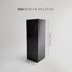 May include: A dark, rectangular object with a textured surface. The object is 6 cm x 6 cm x 17 cm (2.3 in x 2.3 in x 6.6 in). The image shows the object against a plain, light background.
