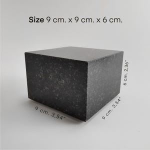 Könnte beinhalten: Ein dunkelgrauer, rechteckiger Block mit gesprenkelter Textur. Die Abmessungen betragen 9 cm x 9 cm x 6 cm (3,54" x 3,54" x 2,36"). Der Block hat eine solide, geometrische Form.