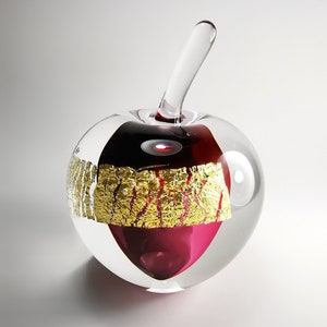 Könnte beinhalten: Eine klare Apfelskulptur aus Glas mit rotem und schwarzem Innenraum und einem klaren Stiel. Der Apfel hat Goldblatt-Akzente. Die Skulptur ist ein dekoratives Kunstwerk.