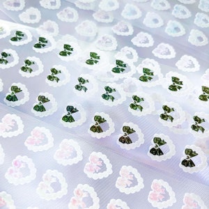 May include: White sheer fabric with a repeating pattern of green bows in white circles. The fabric has a subtle shimmer.