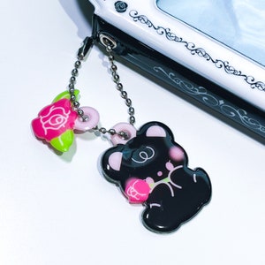 May include: A black bear charm with pink accents holding a pink rose, attached to a silver chain with a pink rose charm.
