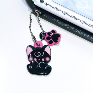 May include: A black cat charm with pink accents and a paw print charm attached to a silver chain.