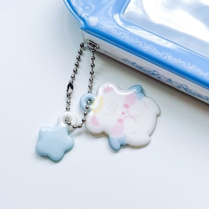 May include: A white ceramic charm with a blue and pink angel design attached to a silver chain with a blue star charm.
