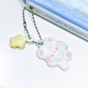 May include: A white and blue charm with a cartoon bear design, attached to a silver chain with a yellow star charm.