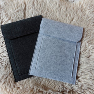 Peut inclure: Deux étuis pour ordinateur portable en feutre, l'un gris et l'autre noir, avec une fermeture à rabat. Les étuis sont posés sur une surface moelleuse de couleur brun clair.