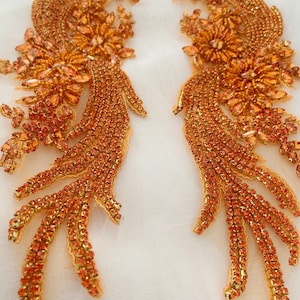 Peut inclure: Deux appliques en perles orange et dorées en forme d'oiseau stylisé avec une longue queue. Les appliques sont faites de petites perles brillantes et sont parfaites pour ajouter une touche d'éclat aux vêtements ou aux objets artisanaux.