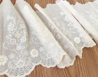 May include: White cotton lace trim with a scalloped edge and delicate floral embroidery. The lace has a subtle sheen and is perfect for adding a touch of elegance to any project.